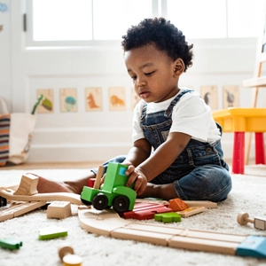 Little boy playing with a wooden, colorful train set while sitting on carpet.