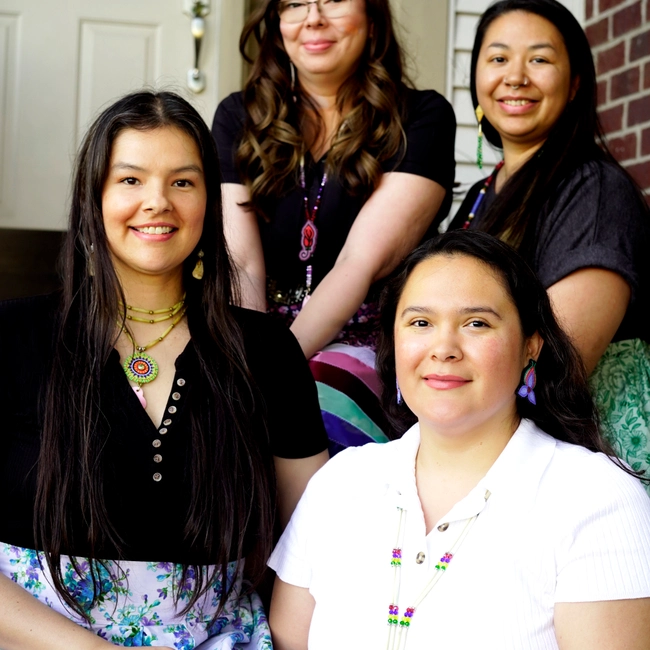 Four women smiling together on a front porch steps.